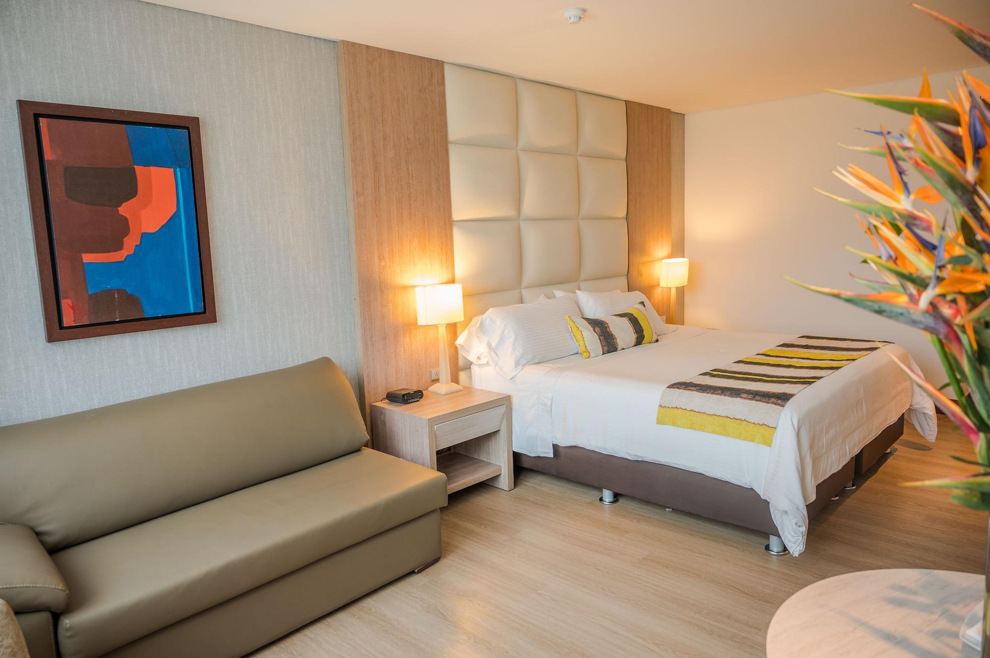 Hotel San Fernando Plaza メデジン エクステリア 写真 The photo shows a stylish hotel room. It features a comfortable bed with decorative pillows and a striped blanket. On either side of the bed, there are bedside lamps providing warm lighting. There is a modern artwork framed on the wall next to the be